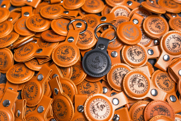 Dozens of tan leather AirTag holders engraved with a company logo