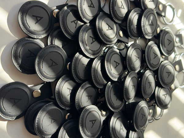 A pile of black leather keychain buttons with a triangular symbol engraved in the center, arranged on a white surface.